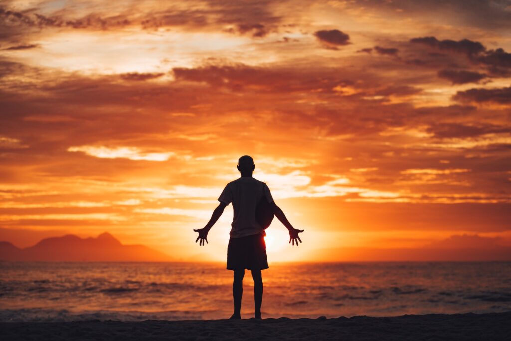 silhouette of man on beach during sunset with his arms outstretched reverentially to existence